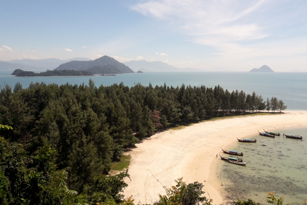 Kuva Thaimaassa olevan pienenestä saaresta, jonka rannalla on kuusi pientä venettä ja yksi ihminen