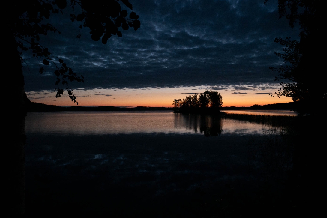Tumma auringonlasku järvenrannalla.